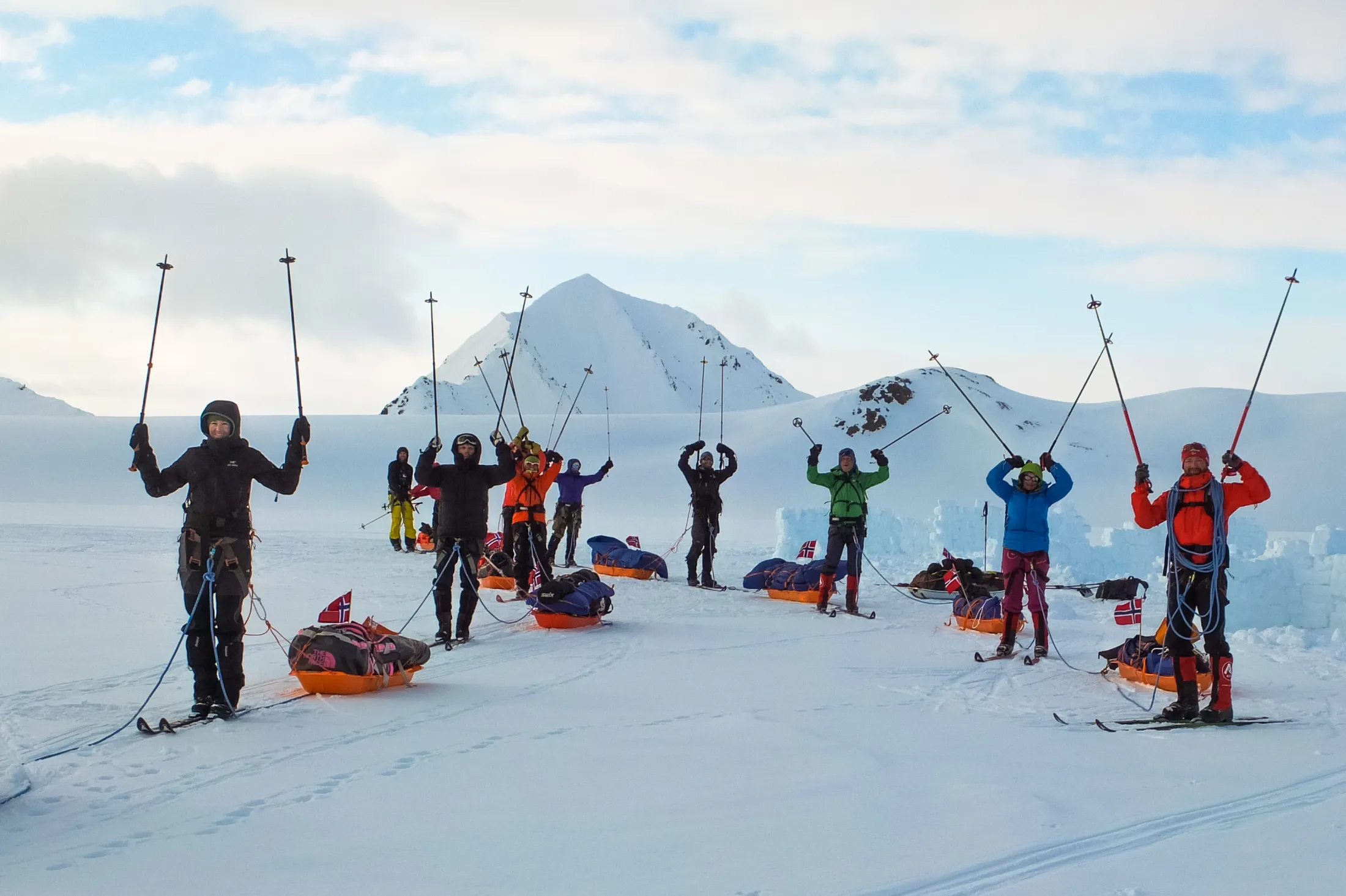 Folk med fjellski og pulk på Svalbard som står med henda i været.