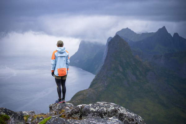 En turgåer står på en fjelltopp og ser ut over dramatiske fjorder og skykledde tinder i Norge.