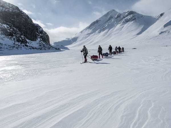 En gruppe skiløpere som trekker pulker gjennom en snødekt fjelldal.