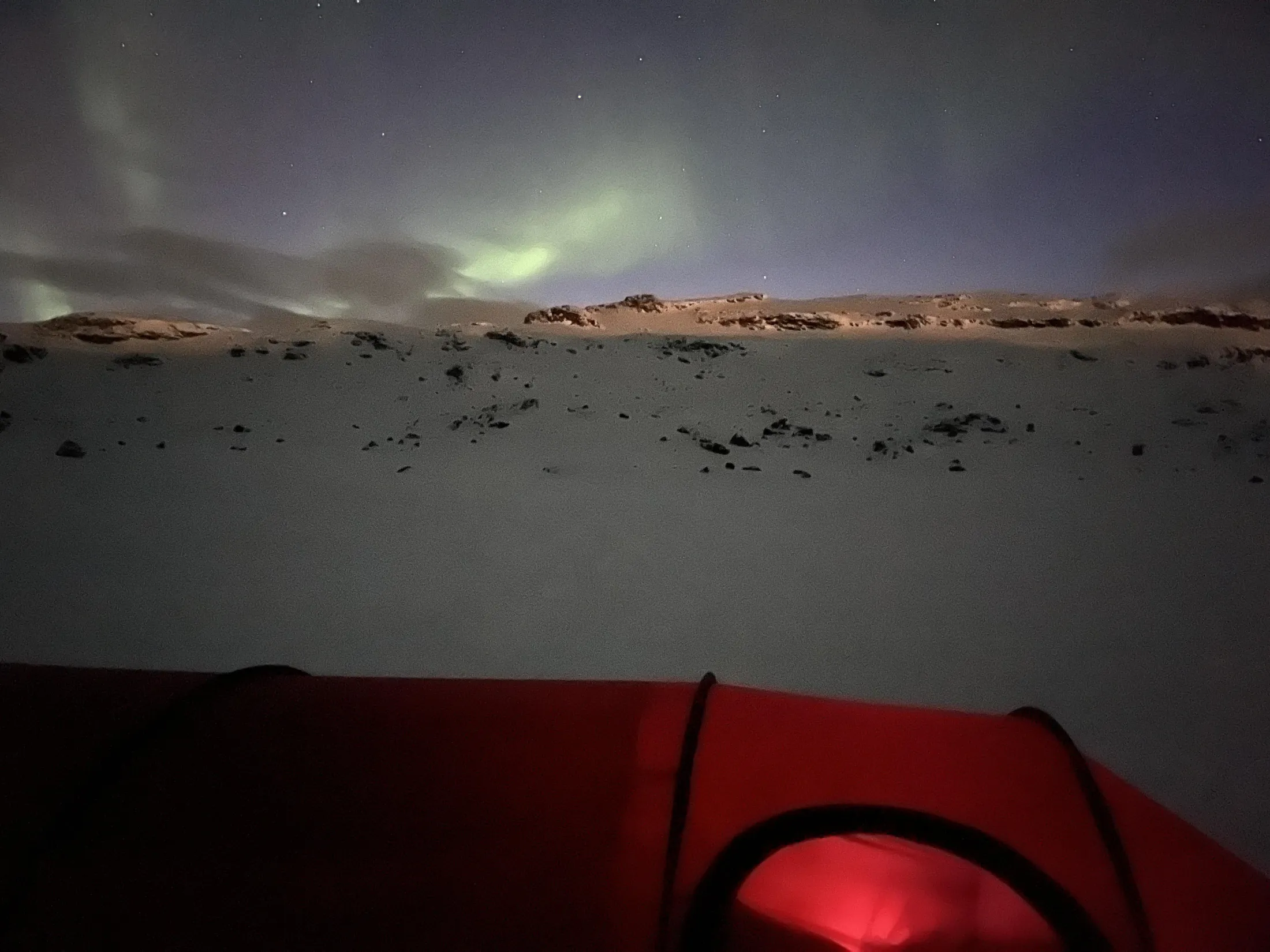 Nordlys over et snølandskap, sett forbi et rødt telt.