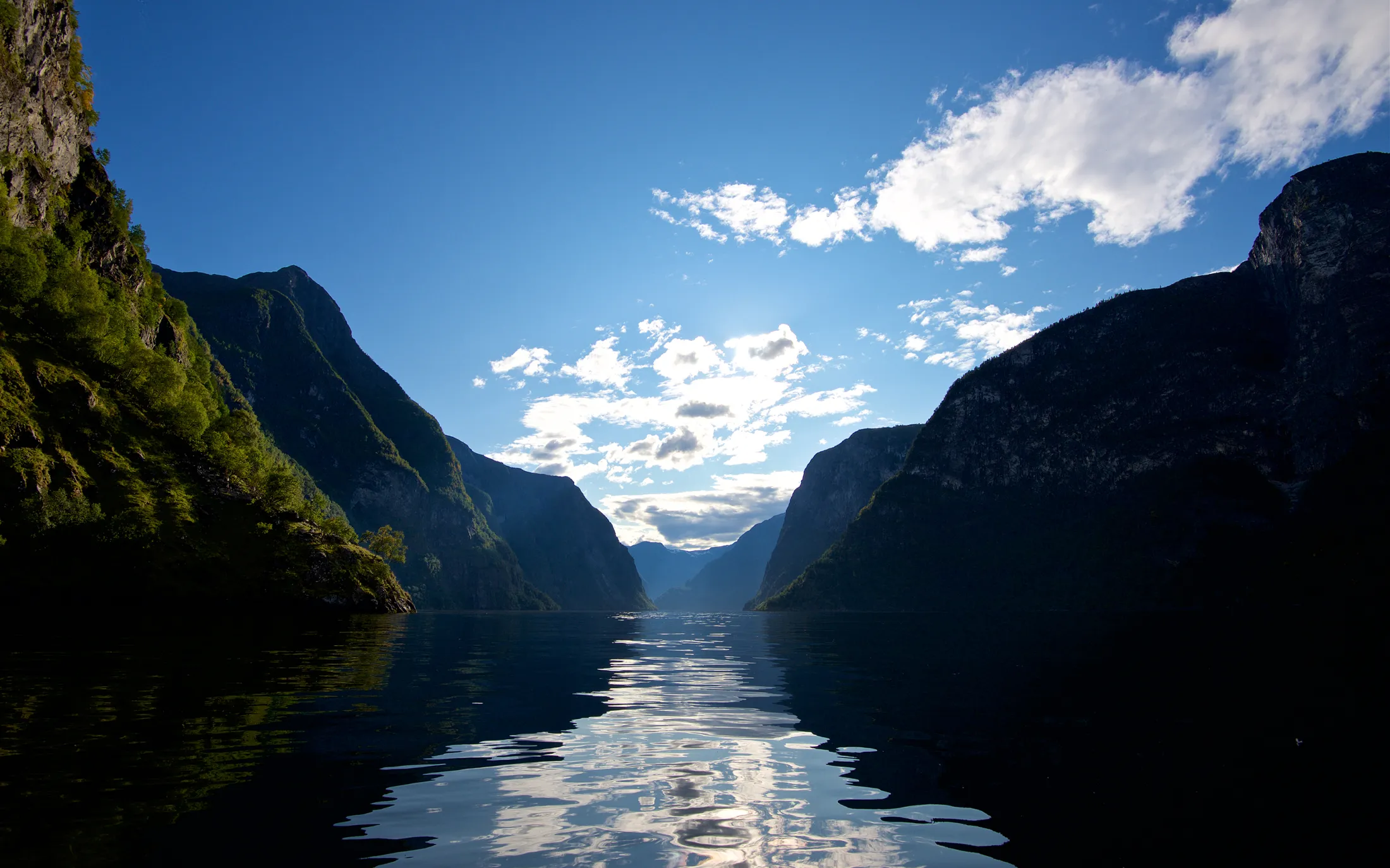 En dyp blå fjord omgitt av bratte fjell under en halvskyet himmel.