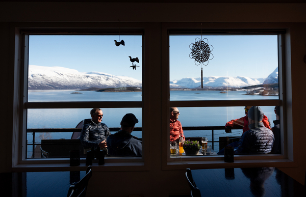 Folk som sitter ved et vindu med utsikt over et vakkert fjell- og havlandskap.