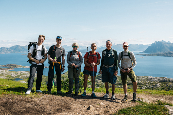 Seks turgåere poserer på en bakketopp med utsikt over sjø og øyer i bakgrunnen.