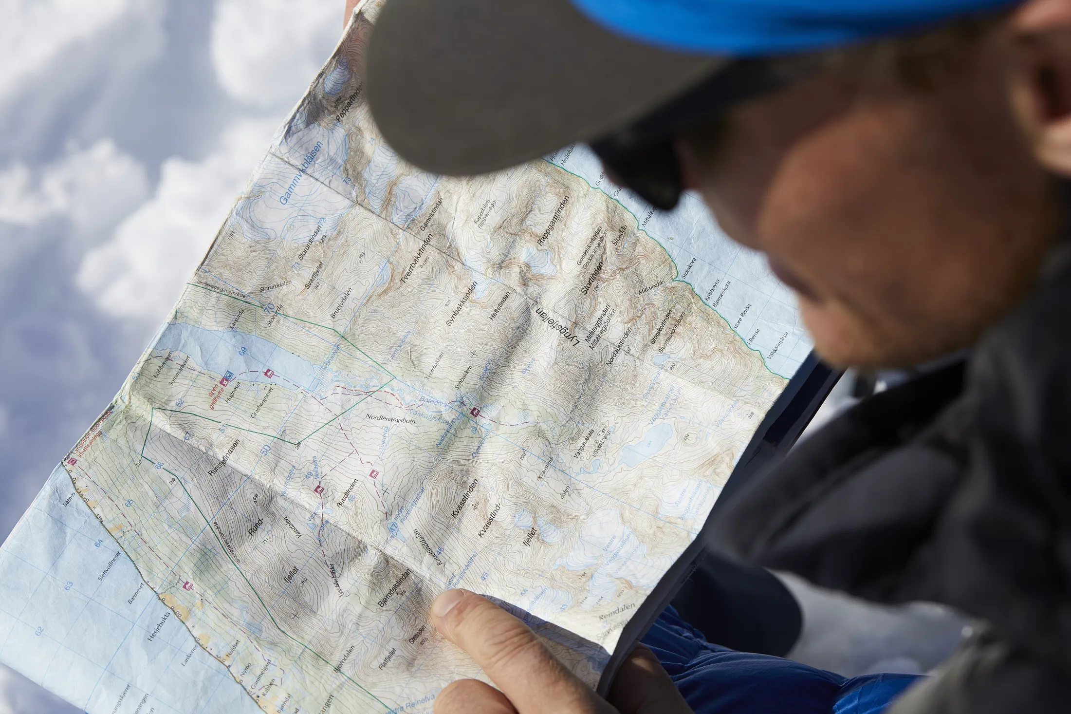 En person med caps og jakke ser nøye på et detaljert topografisk kart utendørs.