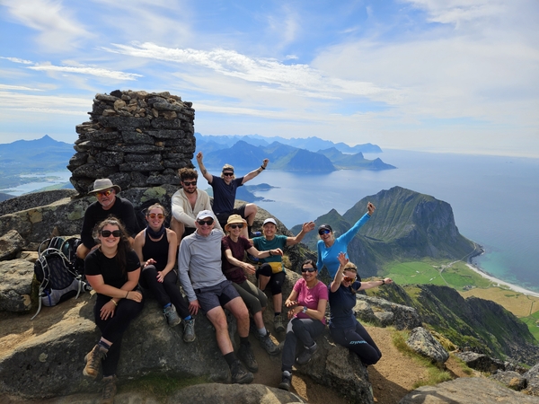 En gruppe turgåere som poserer for et bilde på en fjelltopp med utsikt over hav og øyer.