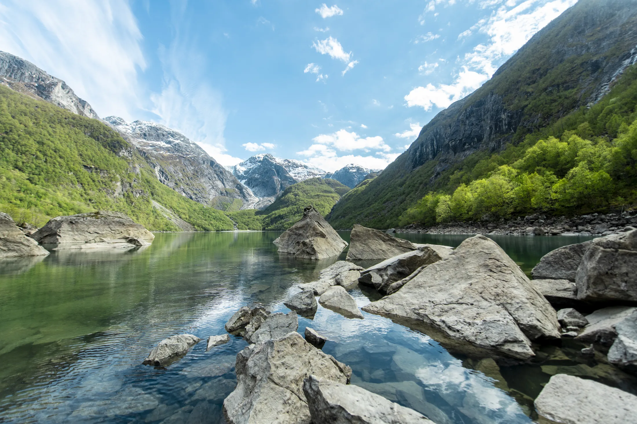 Nydelig fjellvann med klart vann som speiler steiner og omkringliggende grønne skråninger under en blå himmel.