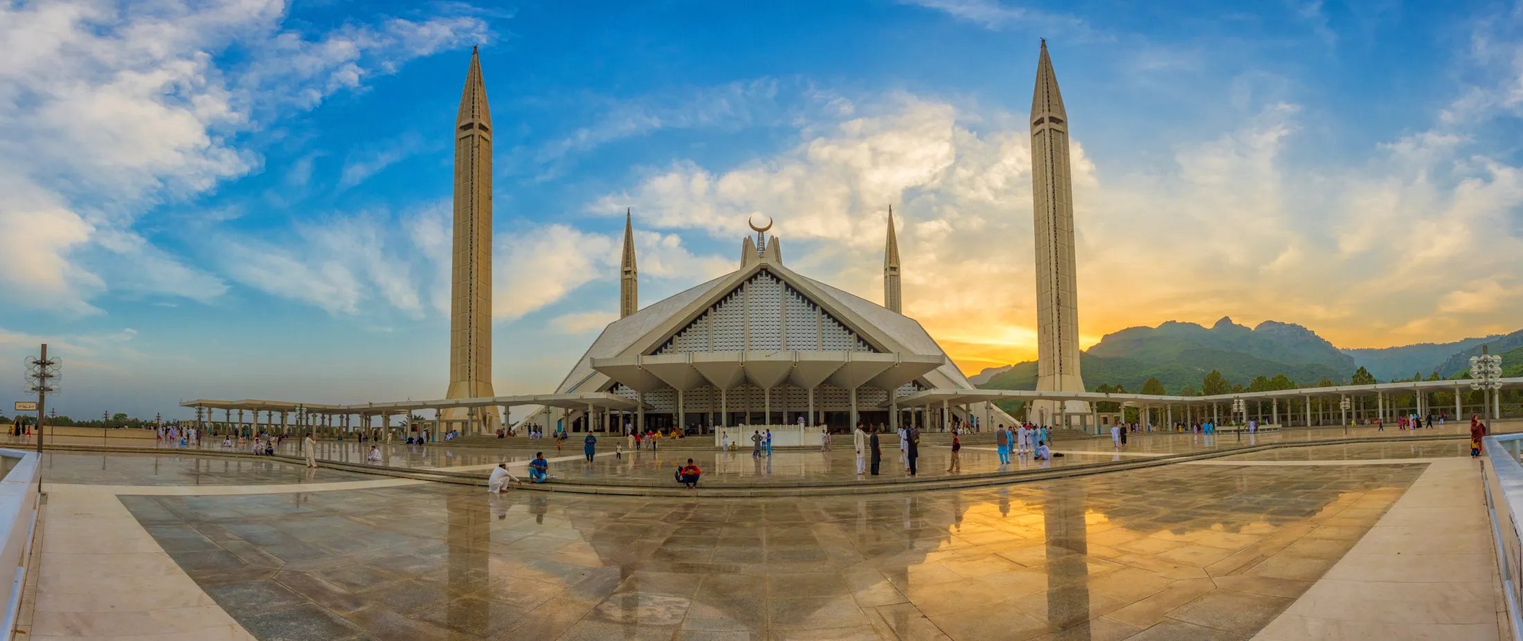 Den storslåtte Faisal-moskeen med sit særpregede, moderne design og høye minareter står opplyst mot en fargerik solnedgangshimmel i Islamabad.