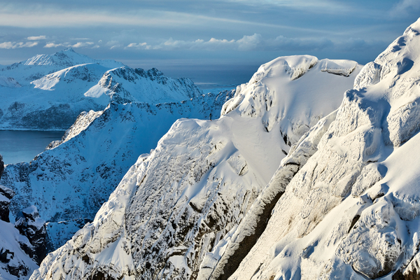 Vinterlandskap med snødekte, forrevne fjelltopper og sollys som treffer de skarpe fjellsidene.