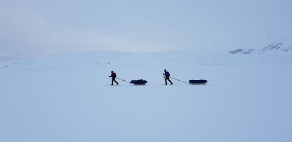 To personer går på fjellski i et snølandskap, og hver trekker en pulk.