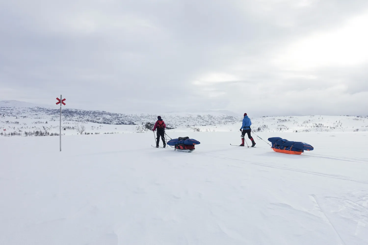 To langrennsløpere med pulk i et snødekt fjelllandskap under en overskyet himmel
