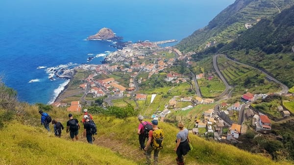 En gruppe turgåere går ned en fjellsti med utsikt over en kystlandsby og det blå havet.