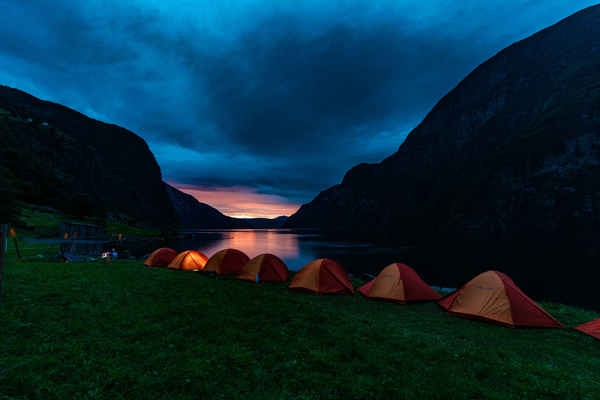 Telt ved fjorden med fjell og solnedgang i bakgrunn.