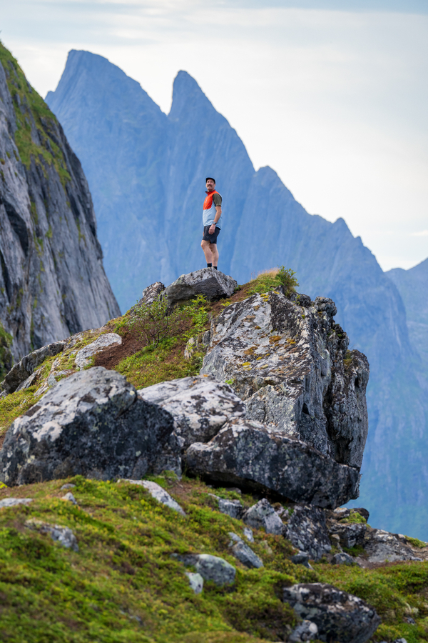 En turgåer som står på en steinete fjellrygg med skarpe topper i bakgrunnen.