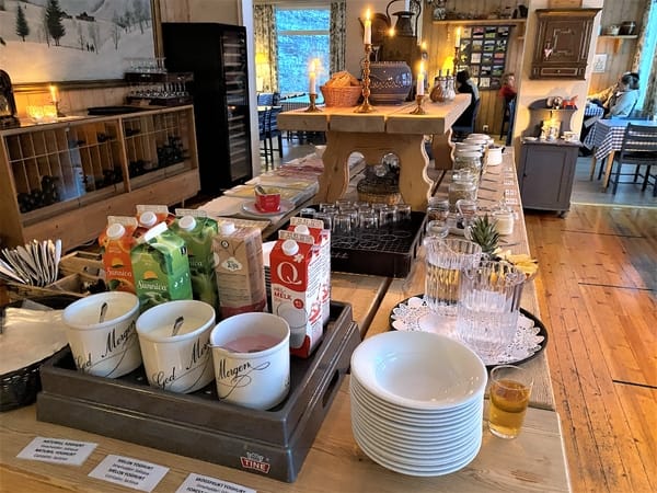 Et koselig kaféinteriør med en tredisk som viser kopper, juicekartonger og stablede skåler.