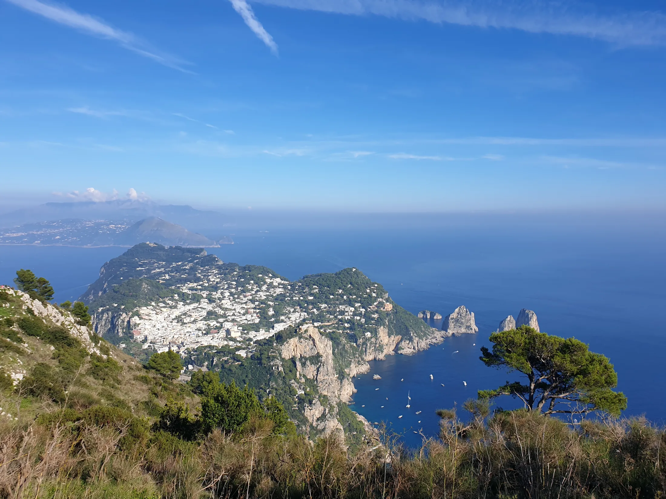 Høyt perspektiv av øya Capri med sine hvite bygninger, steinete klippevegger og blått hav under en klar himmel.