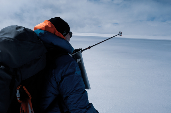 En person med sekk peker med en skistav i et snølandskap.
