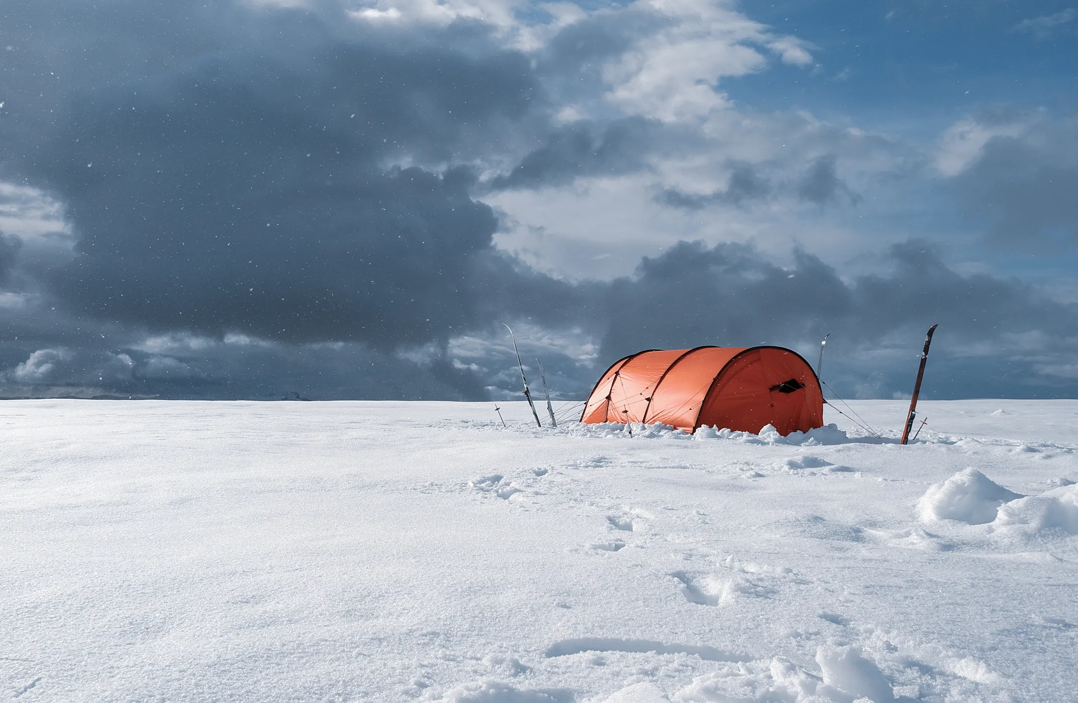 Et oransje telt satt opp i et snødekt landskap under en dramatisk, skyet himmel.