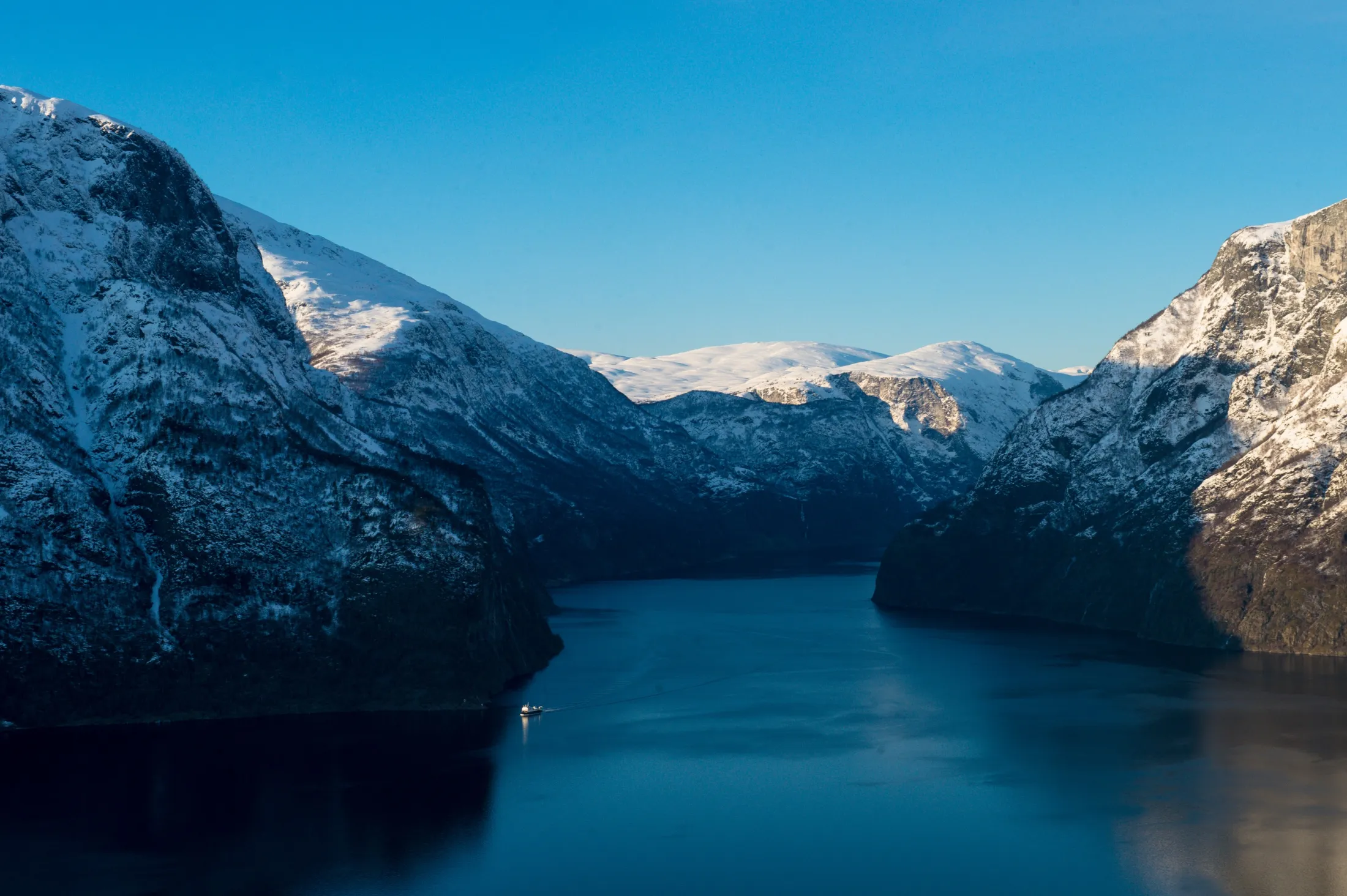 Snødekte fjell som omgir en dyp blå fjord under en klar himmel.