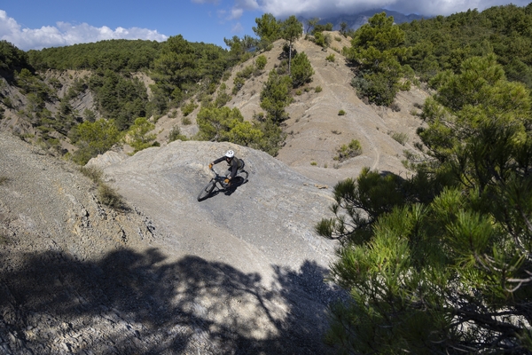 En terrekampsyklist som navigerer i en bratt, grusete skråning i et skogkledd fjellandskap.