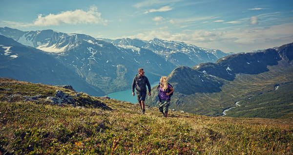To personer på fjelltur i et landskap med fjord i bakgrunnen.