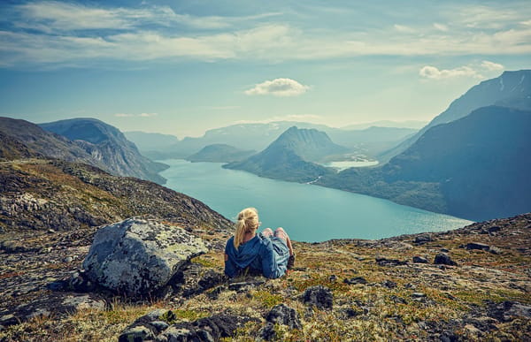 En person sitter på en fjellrygg og ser ut over en fjord og et fjelllandskap.