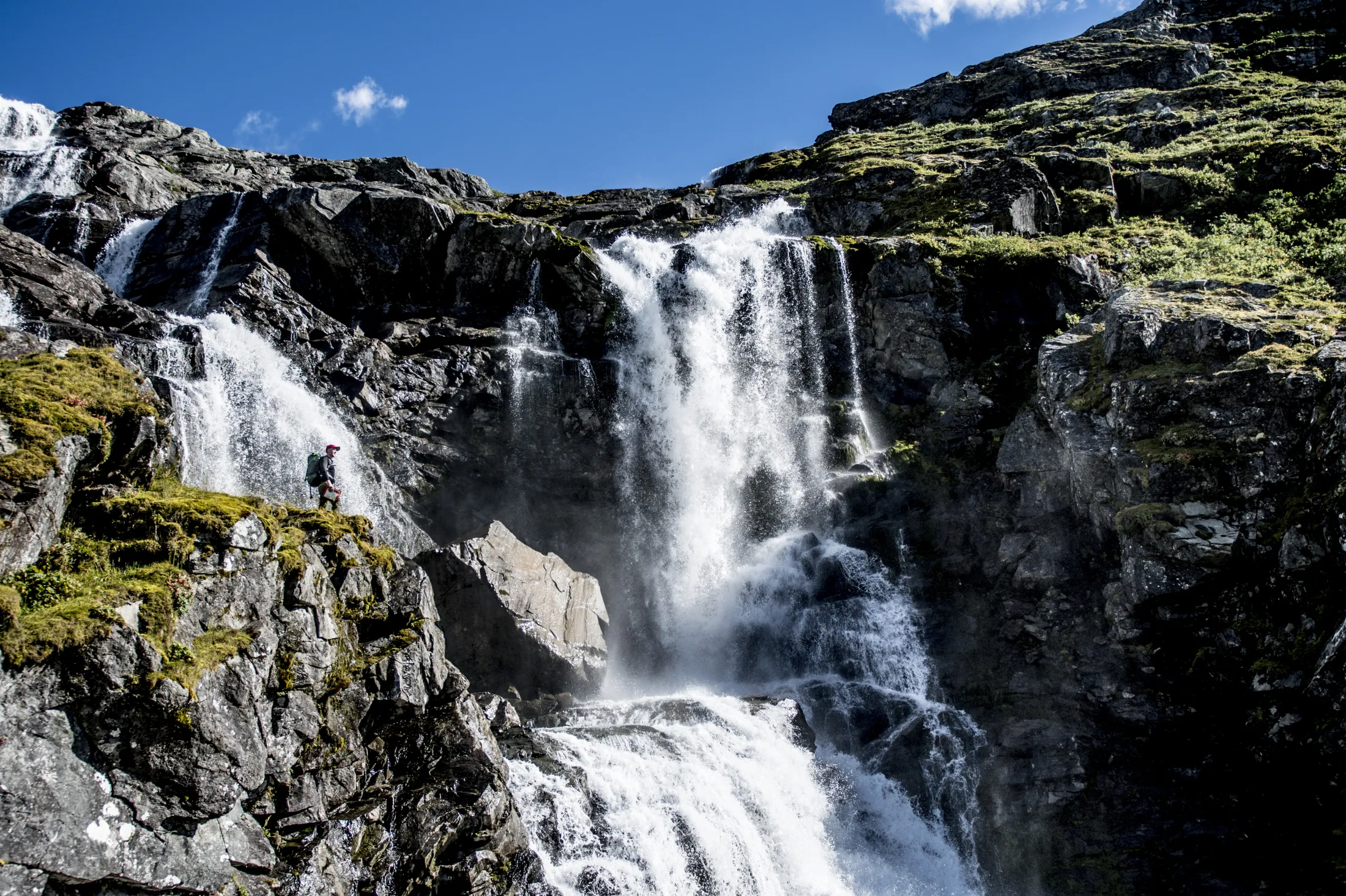 En kraftig foss som fosser nedover forvridde fjellskrenter under en klar blå himmel.