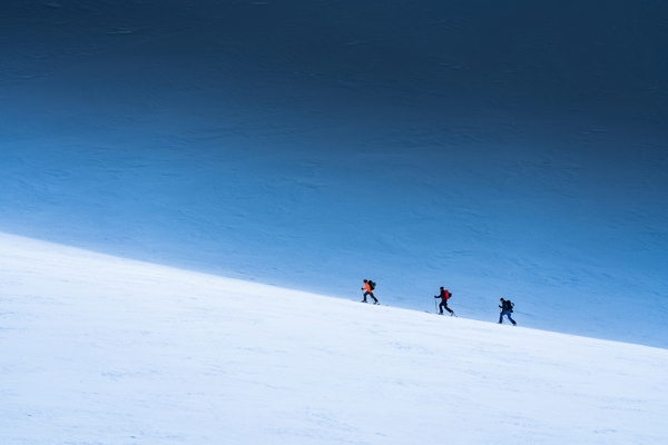 Tre personer som går på en snødekt skråning under en blå himmel.