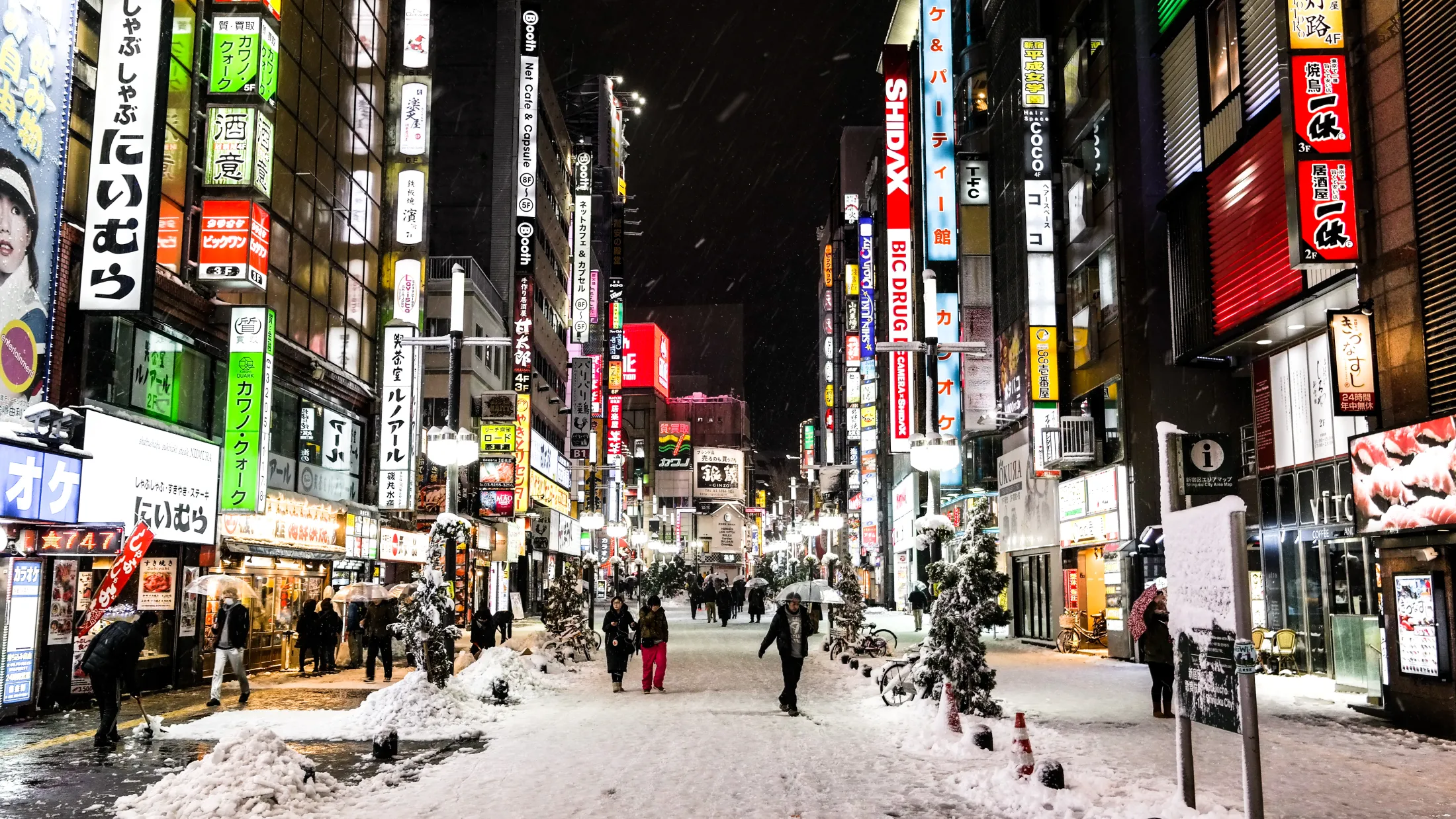 En snødekt gate i en japansk storby, med høye bygninger og reklameskilt på hver side.
