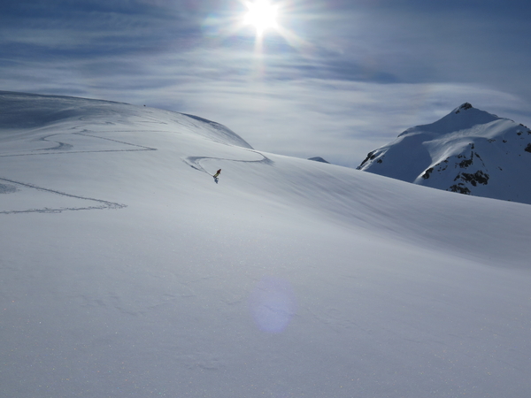 En ensom skiløper på en stor, snødekt fjellside under en sterk sol.
