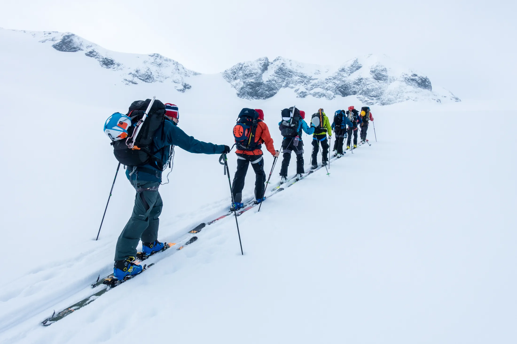 En gruppe skiløpere som går på tur på ski i enerad over et snødekt landskap med fjell i bakgrunnen.