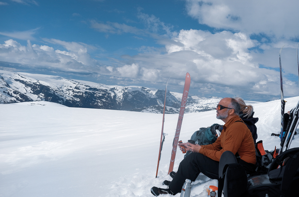 En mann som hviler på ski i et snødekt fjellandskap under en skyet himmel.