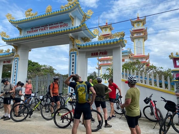 En gruppe syklister med sykler som står utenfor en tempelport i Vietnam.