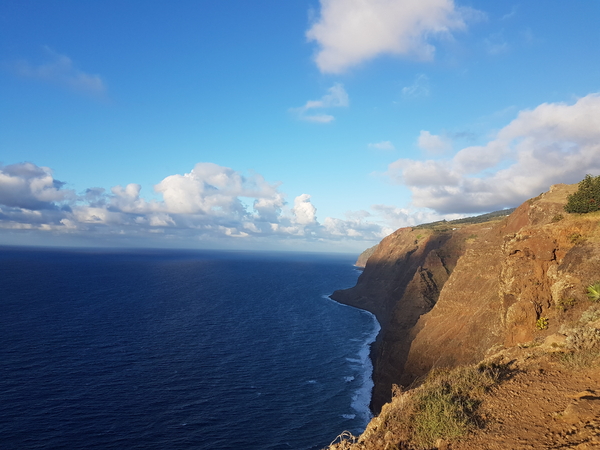 Bratte klipper som møter det dype blå havet under en delvis skyet himmel.