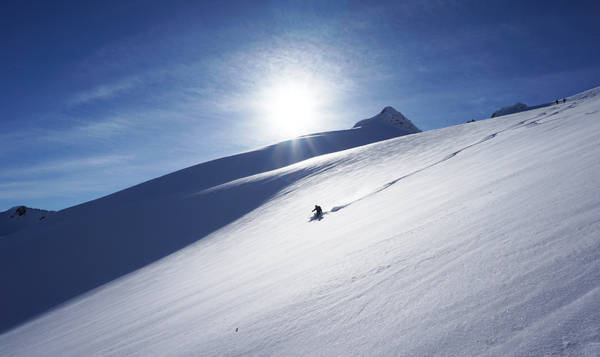 En skiløper på en stor, snødekt fjellside under en klar sol og blå himmel.