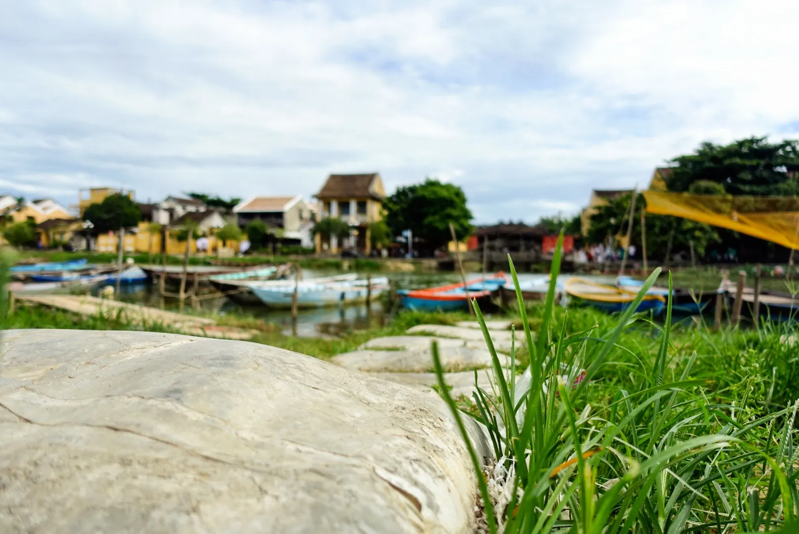 Båter fortøyd langs en elvebredd i Hoi An, Vietnam, med tradisjonelle hus i bakgrunnen.