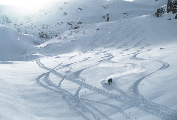 En skiløper som svinger i dyp pudbersnø med synlige skispor på kryss og tvers i bakken.