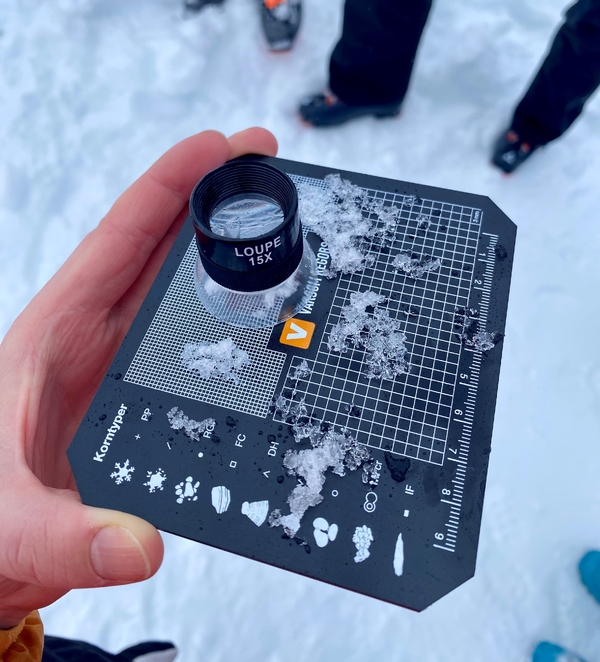 En person holder et snøprofilbrett med forstørrelsesglass og snøprøver på.