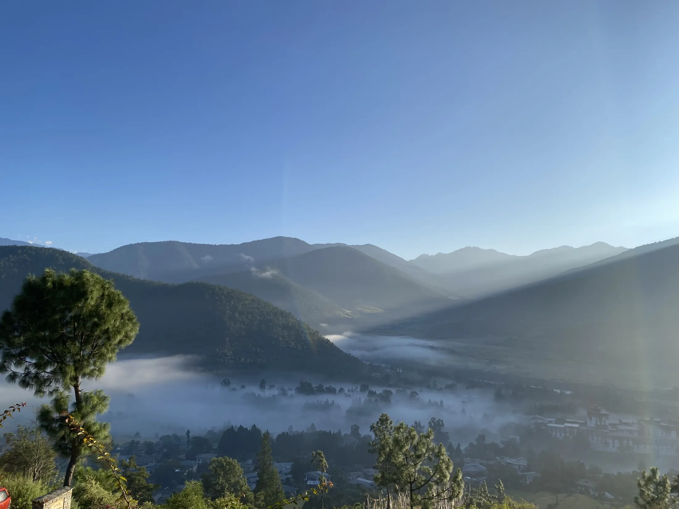Sollys som skinner over lagdelte fjellrygger og lyser opp en tåkefylt dal om morgenen.