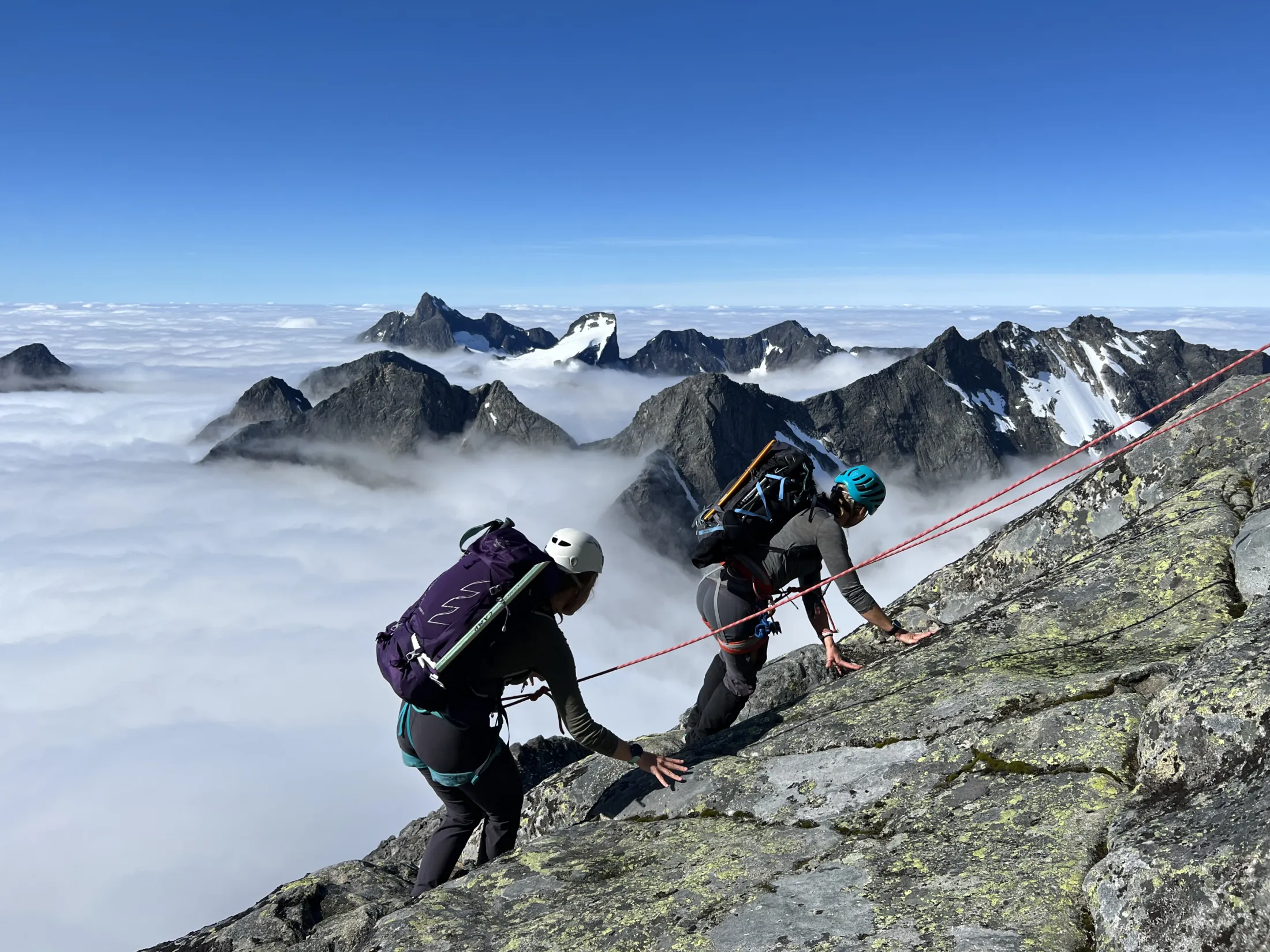To fjellklifrere som klatrer på en steinete eg over et skyhav.