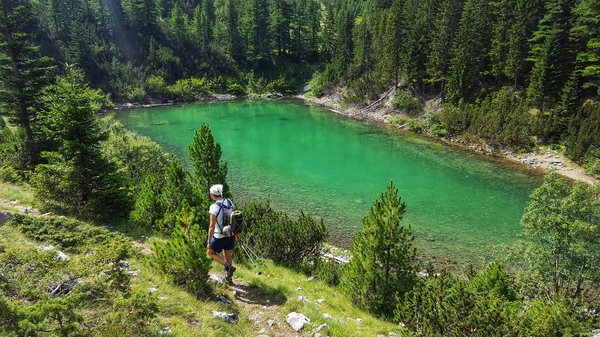 En turgåer som ser på et fantastisk smaragdgrønt fjellvann omgitt av tett grønn skog.