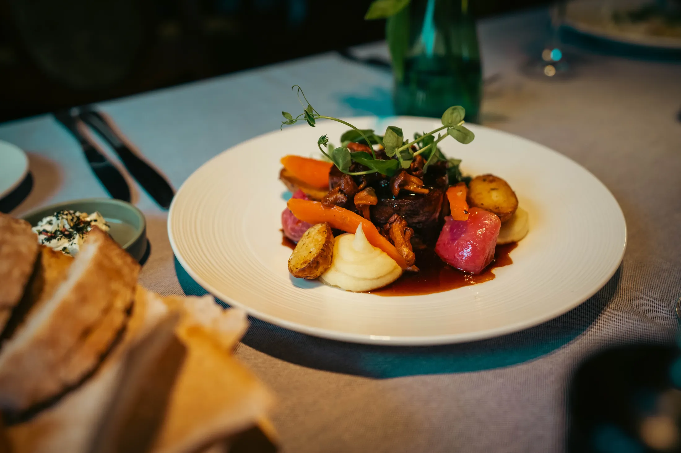 En deilig middagstallerken i hvit, med ovnstekte grønnsaker, kjøtt, brun saus og grøn garnityr på toppen.