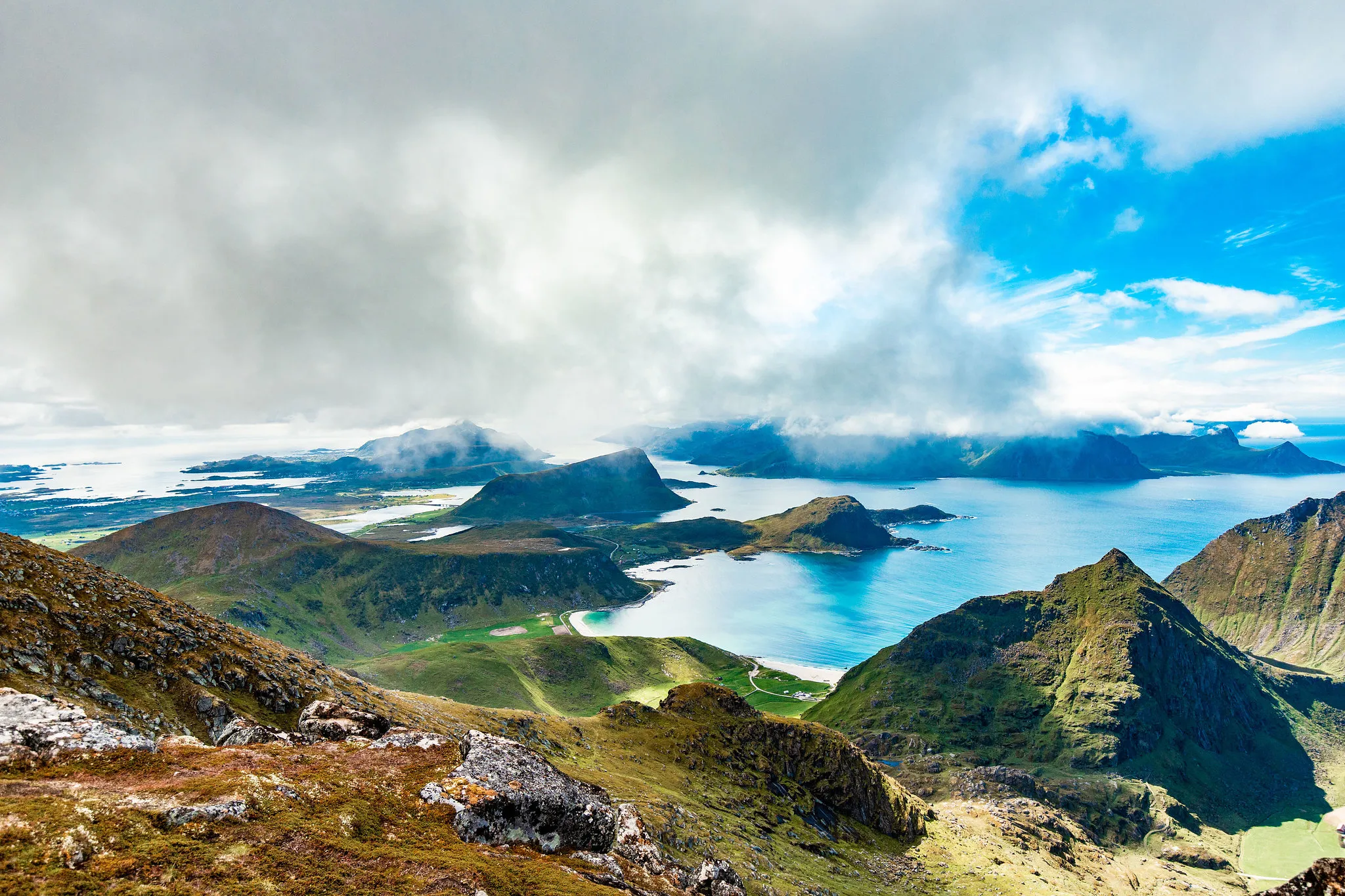 Panoramautsikt fra luften av dramatiske fjelltopper som møter havet under en skyet himmel i Lofoten.