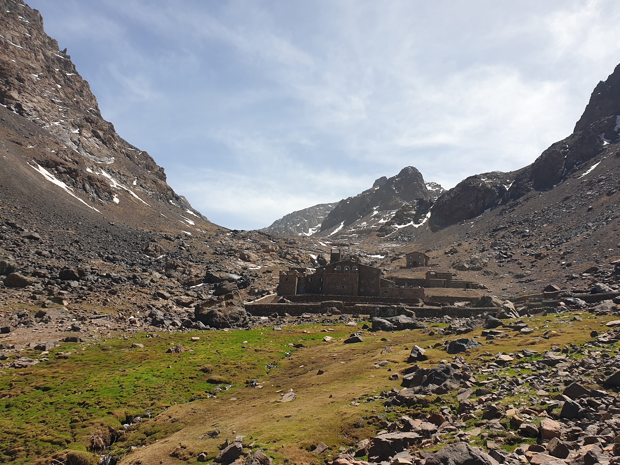 En stenbygning i midten av fjellene med en gressflekk forran