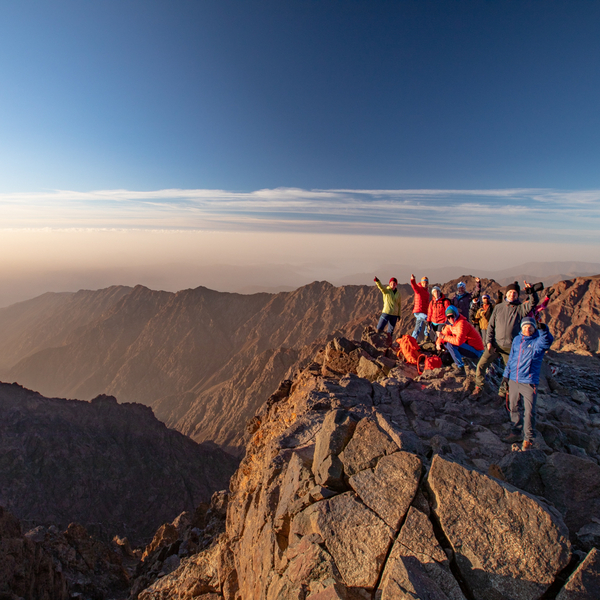 Gruppe mennesker som står på toppen av et fjell med blå himmel